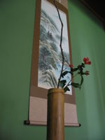 A chabana flower arrangement in front of a hanging scroll